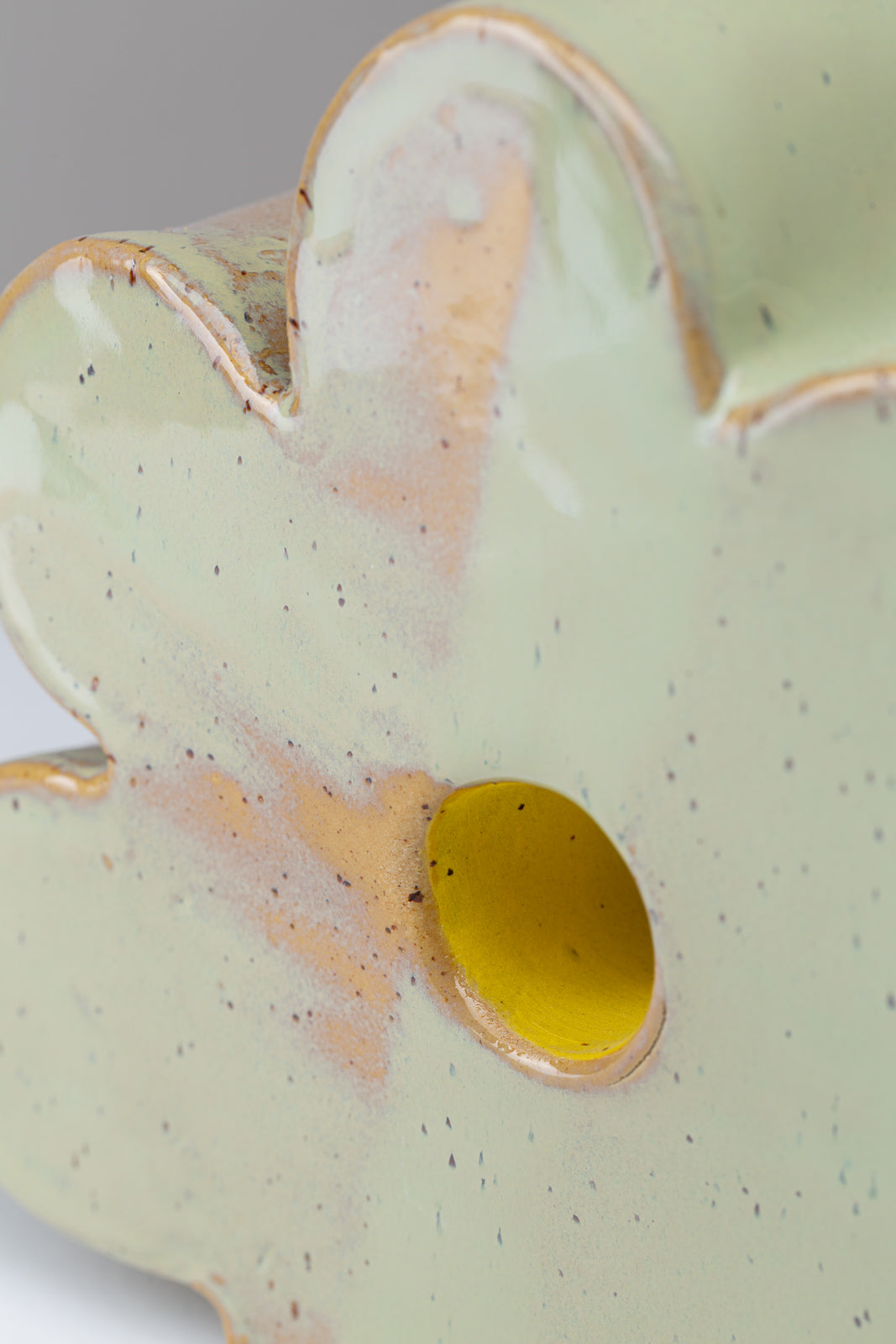 Man sieht die Nahaufnahme einer Vase in Form einer Blume, die Vase ist hellgrün mit Pünktchen und einem gelben Akzent in der Mitte