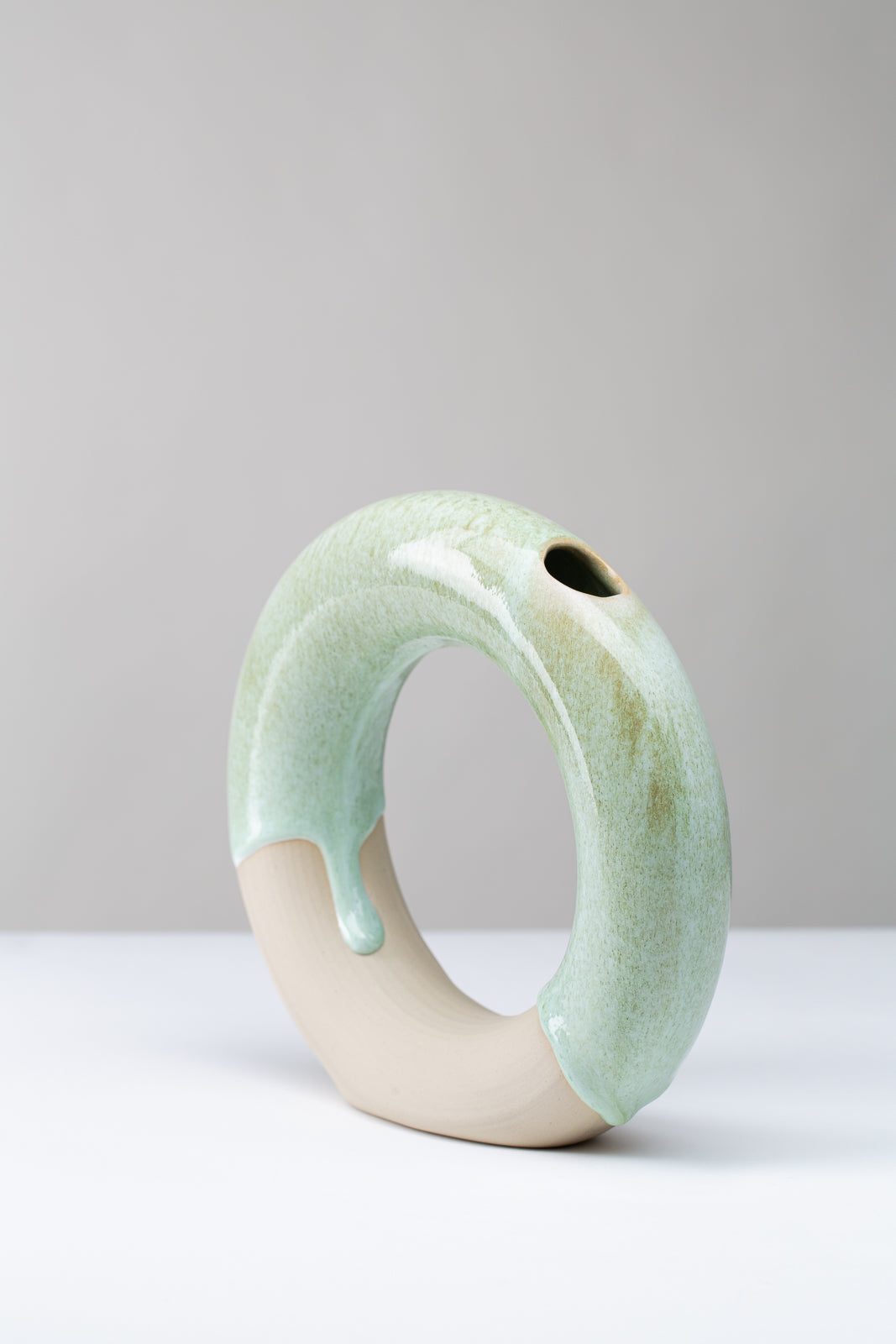 runde Vase in der Form eines Ringes auf weißem Hintergrund, die Farbe der Vase sind Grüntöne, man sieht die Vase von der Seite und die Öffnung für die Blumen